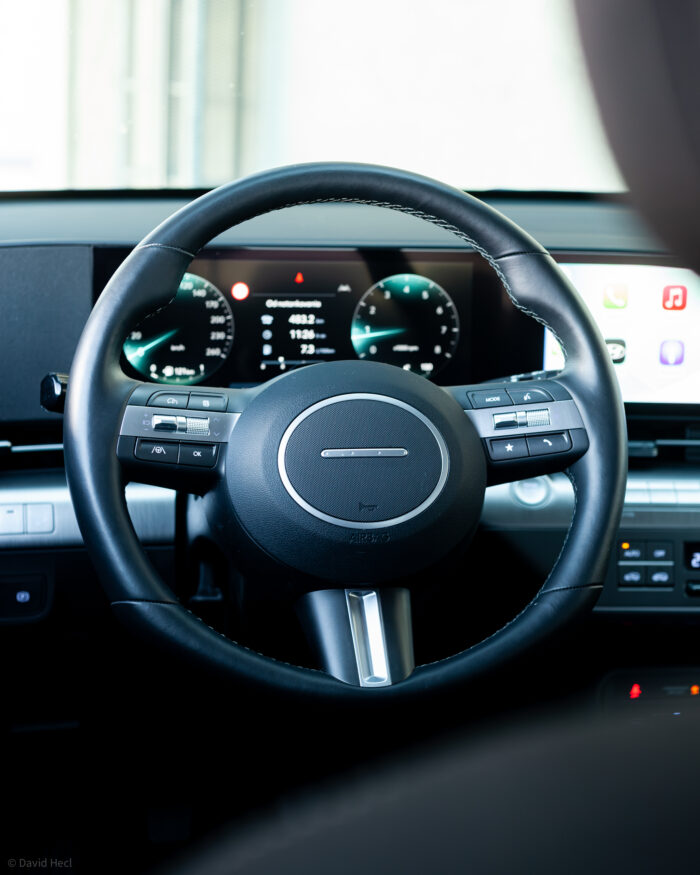 Autobazar.EU | V interiéri je to absolútna klasika. Volant s logickým usporiadaním prvkov na ovládanie systému má príjemnú hrúbku venca. Čo sa mi páči je, že Hyundai umožňuje deaktiváciu výstrahy pred prekročením rýchlosti priamo na volante. Nemusím sa teda hrabať hlboko v infotainmente, ako to je, bohužiaľ, pri niektorých autách potrebné. Za volantom je klaster dvojice prepojených displejov, ktorý poznáme z modelov IONIQ.
